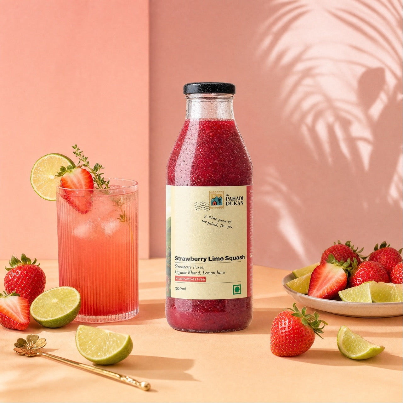 Bottle of strawberry lime squash with a glass of juice and fresh fruits on a pink background
